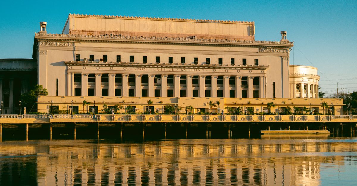 Capture of the iconic Manila Post Office, reflecting in the tranquil Pasig River under a clear sky.